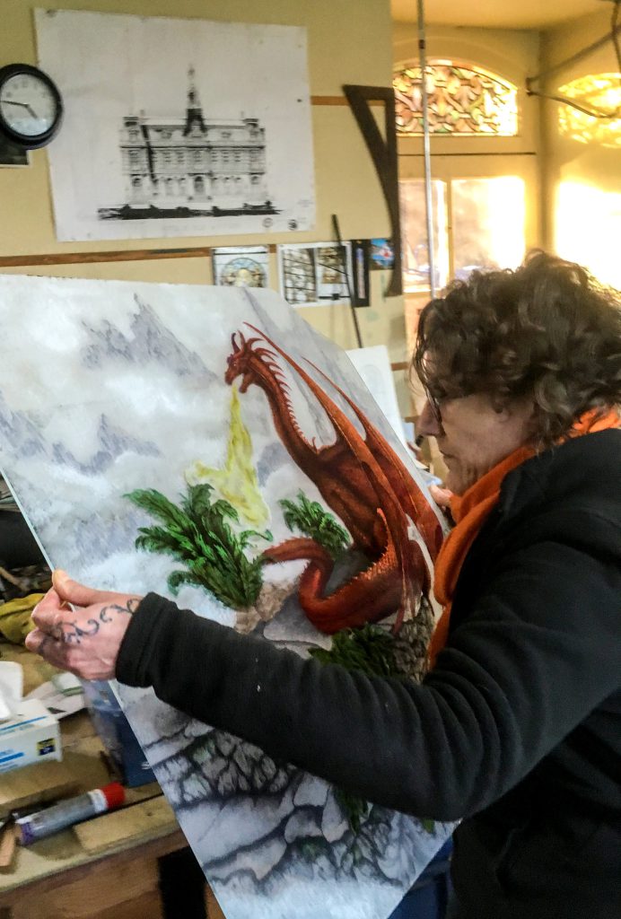 Françoise Théallier tenant dans ses mains un vitrail au motif de dragon réalisé pour un particulier, en décor de maison